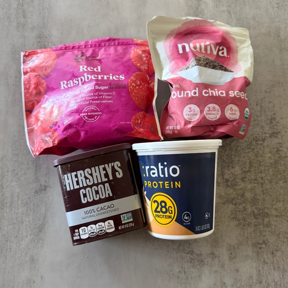 Ingredients for high-protein chocolate raspberry fluff with vanilla protein yogurt, raspberries, chia seeds, and cocoa powder.